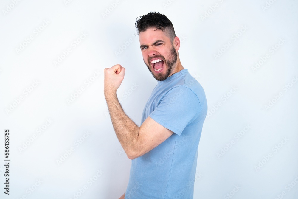 Profile side view portrait Young caucasian man wearing blue T-shirt over white background celebrates victory Profile side view portrait Young caucasian man wearing blue T-shirt over white background celebrates victory