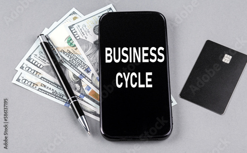 Credit card and text BUSINESS CYCLE on smartphone with dollars and pen. Business