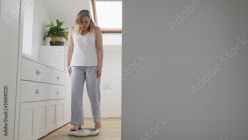 Menopausal Mature Woman Concerned With Weight Gain Standing On Scales In Bedroom At Home