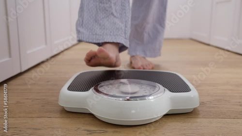 Close Up Of Menopausal Mature Woman Concerned With Weight Gain Standing On Scales In Bedroom At Home
