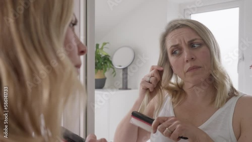Menopausal Mature Woman Suffering Hair Loss Brushing Hair Reflected In Mirror At Home