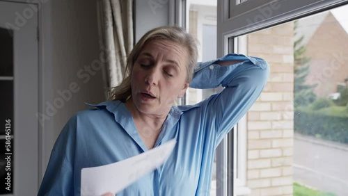 Menopausal Mature Woman Having Hot Flush At Home Cooling Herself With Letters Or Documents