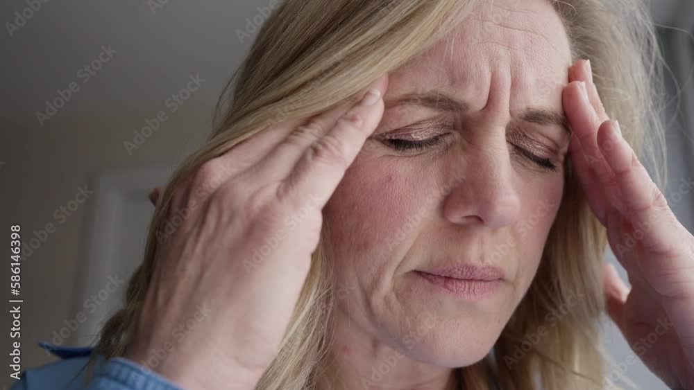 Menopausal Mature Woman At Home Standing By Window Suffering With Headache Or Migraine Pain Menopausal Mature Woman At Home Standing By Window Suffering With Headache Or Migraine Pain
