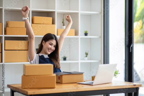 Happy young Asian woman entrepreneur, Smile for sales success after checking order from online shopping store in a smartphone at home office, Concept of merchant business online and eCommerce