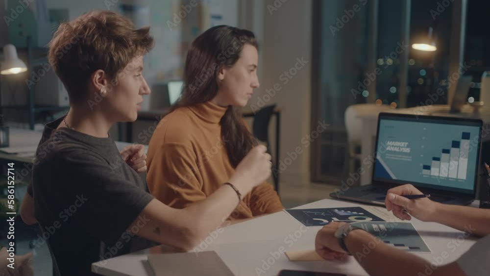 Business team having discussion during night meeting in the office, using laptop and paper slides. Medium shot, overworking concept Business team having discussion during night meeting in the office, using laptop and paper slides. Medium shot, overworking concept