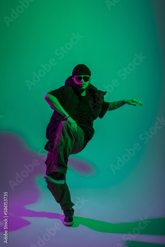 Cool fashion professional dancer man with sunglasses in black stylish clothes dancing in creative color studio with green and pink light © alones