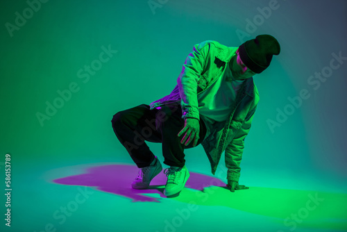 Fashionable handsome young b-boy man dancer with cap in fashion denim clothes dancing in creative studio with green and pink color