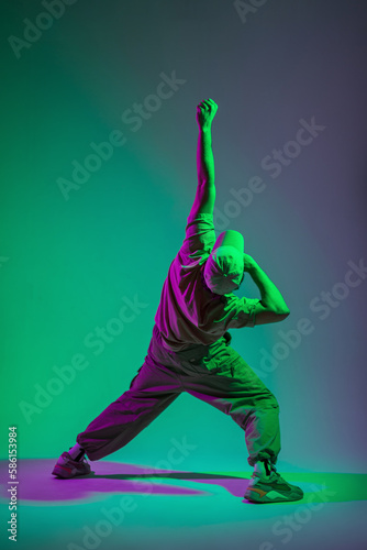 Fashionable handsome stylish man model dancer in trendy fashion clothes with cap dancing in creative color studio with magenta and cyan light © alones