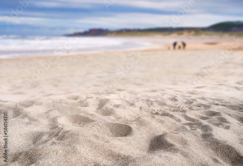 A coastal foreground texture scene to place products on the sand with a blurred sea background on a sunny summer day.