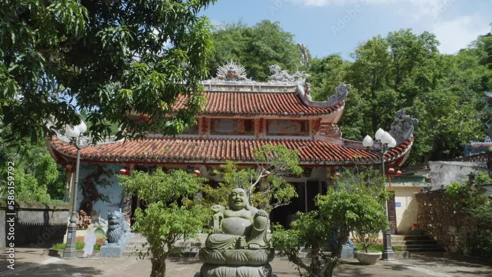 Buddhist temple in Marble Mountain, Da Nang, Vietnam. In front of the entrance to the temple is a statue of a fat Buddha. tilt up shot. Buddhist temple in Marble Mountain, Da Nang, Vietnam. In front of the entrance to the temple is a statue of a fat Buddha. tilt up shot.