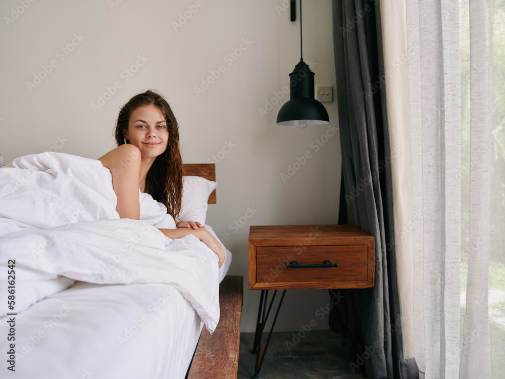 A woman after a shower with wet hair lies on a bed under a blanket in a bedroom near a window, a healthy sleep on an orthopedic mattress and a memory foam pillow, body and hair care A woman after a shower with wet hair lies on a bed under a blanket in a bedroom near a window, a healthy sleep on an orthopedic mattress and a memory foam pillow, body and hair care