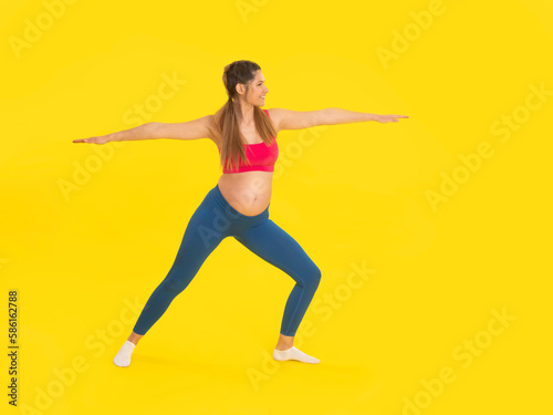 Young pregnant woman doing pilates exercise with stretched hand and leg