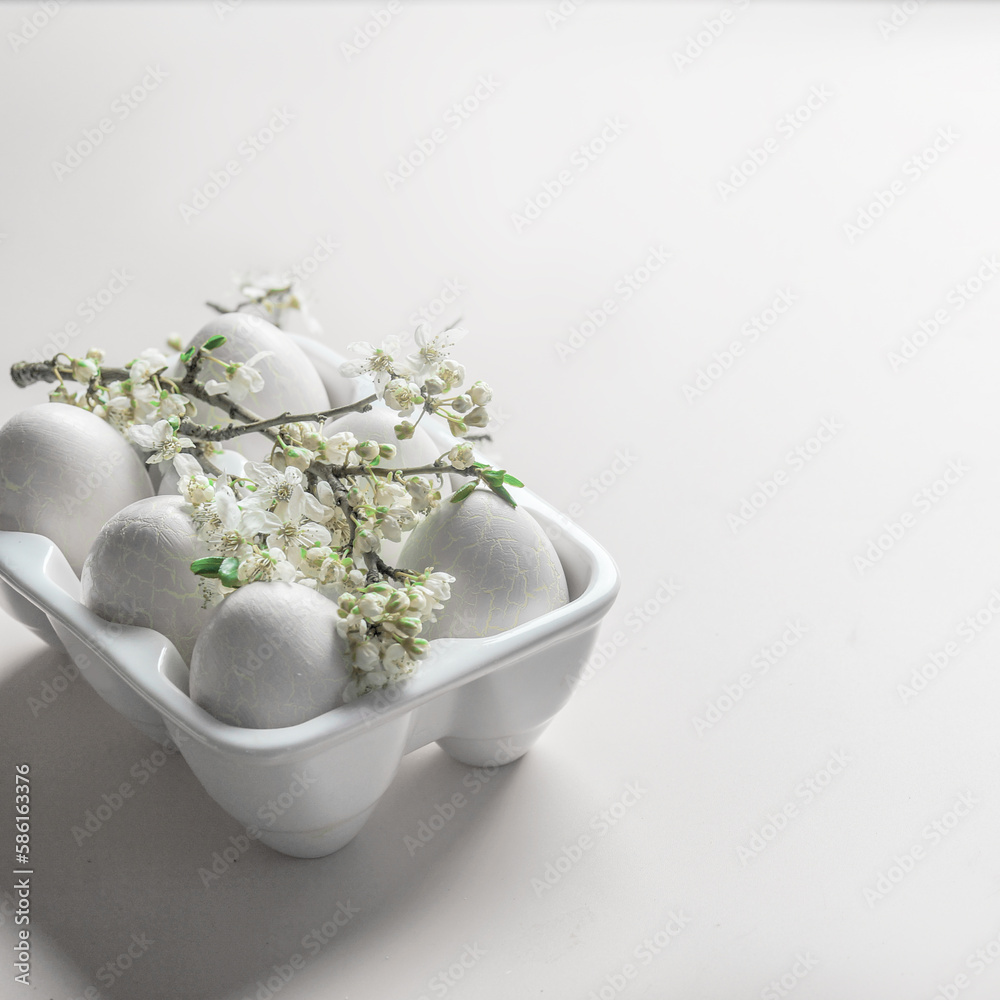 Easter background with eggs in white holder and springtime cherry blossom branch with green leaves Easter background with eggs in white holder and springtime cherry blossom branch with green leaves