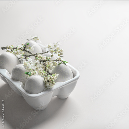 Easter background with eggs in white holder and springtime cherry blossom branch with green leaves