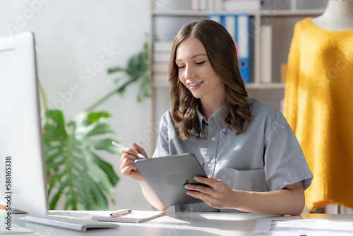 Female fashion designer sitting happily working on tablet.