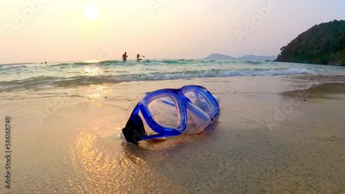 Asian woman grabs snorkel mask on the beach while running into the ocean during beautiful sunset. Summer holidays, relaxing vacation beach trip at seaside. Scuba equipment. Travel advertising.