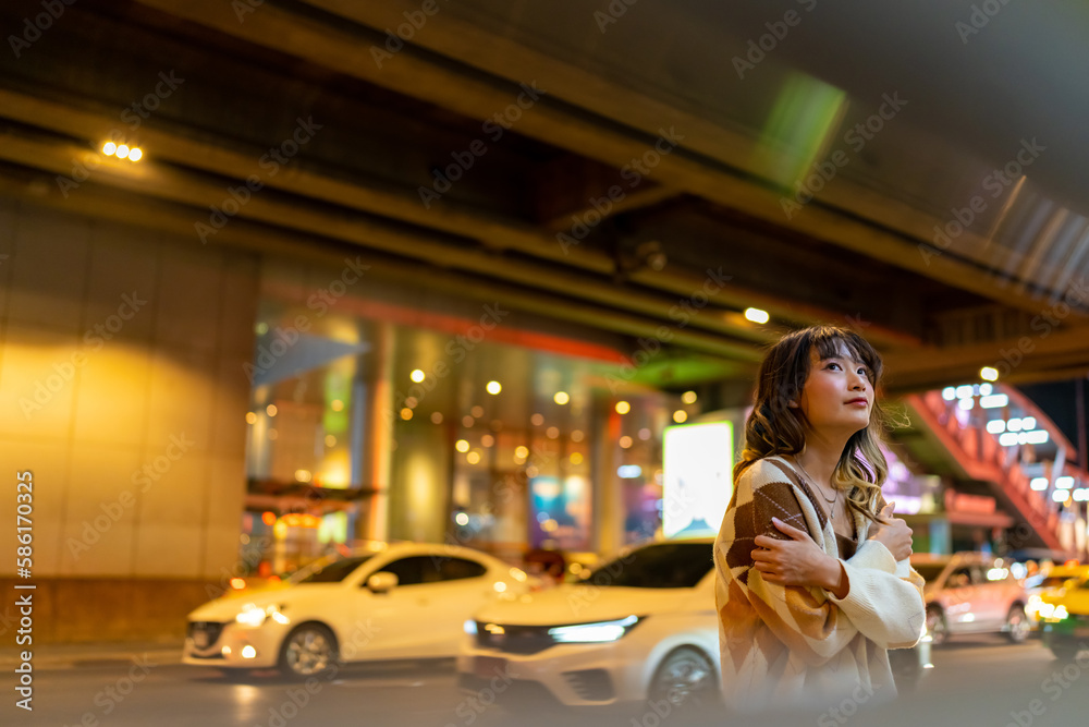 Portrait of Young Asian woman looking cityscape building with street light during travel city street at night. Attractive girl enjoy and fun outdoor lifestyle shopping in the city on holiday vacation.