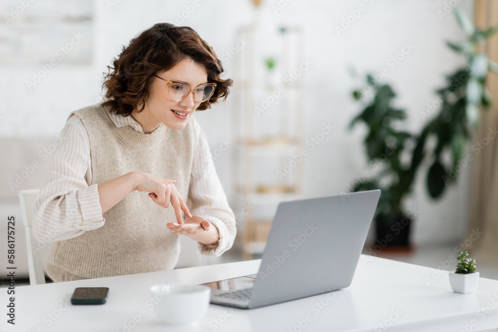 curly woman showing stand word while teaching sign language during online lesson on laptop. - obrazy, fototapety, plakaty 