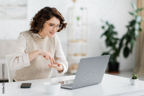 curly woman showing stand word while teaching sign language during online lesson on laptop. photo