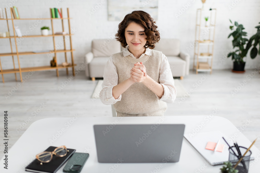 smiling woman showing friendship gesture while using sign language during online lesson on laptop at home. smiling woman showing friendship gesture while using sign language during online lesson on laptop at home.