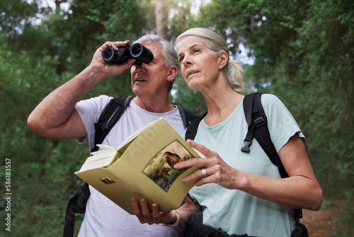 Book, bird watching and binoculars with old couple in nature for bonding, discovery and travel adventure. Search, hiking and view with senior man and woman in forest for explore, retirement and hobby