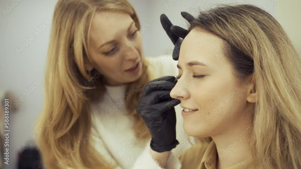 Portrait of a young woman whose eyebrows are plucked with tweezers in a beauty salon, she talks with the master during the procedure. beauty industry. Portrait of a young woman whose eyebrows are plucked with tweezers in a beauty salon, she talks with the master during the procedure. beauty industry.