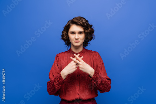 young teacher looking at camera and showing gesture in sign language isolated on blue. © LIGHTFIELD STUDIOS