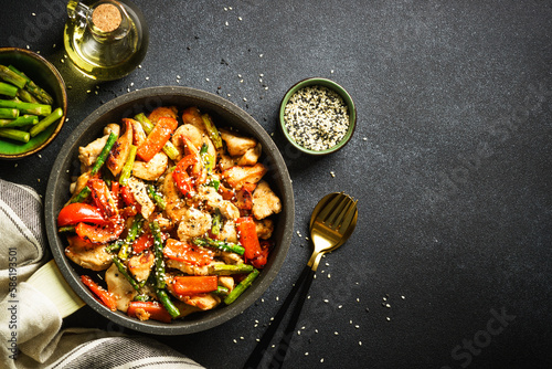 Chicken stir fry with vegetables in the skillet at black stone background. Top view with copy space.