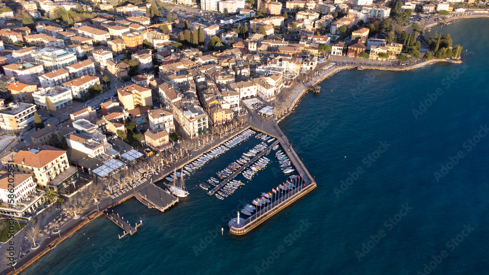 Obraz premium Aerial view with drone of the city of Garda. Town on the lake of the same name, blue sea at sunset, seagulls and boats in the distance.