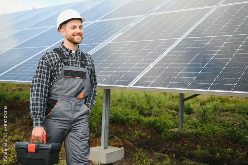 Male worker in uniform outdoors with solar batteries at sunny day.