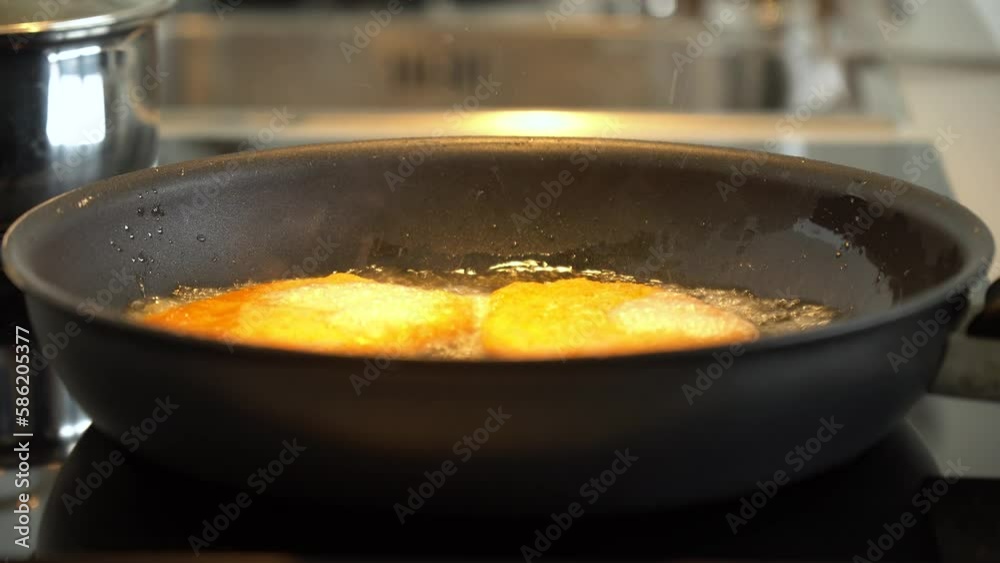 A chicken schnitzel is tossed onto a pan sizzling with hot oil - closeup A chicken schnitzel is tossed onto a pan sizzling with hot oil - closeup