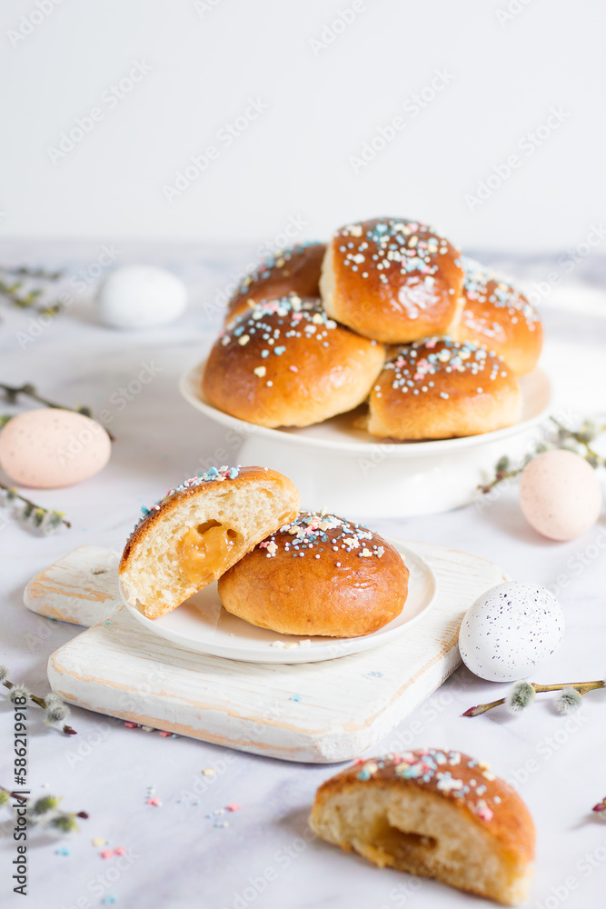Easter buns with caramel filling. The foreground is in blur, the middle plan is a section of a bun. On a light background with Easter attributes - eggs and willow branches Easter buns with caramel filling. The foreground is in blur, the middle plan is a section of a bun. On a light background with Easter attributes - eggs and willow branches