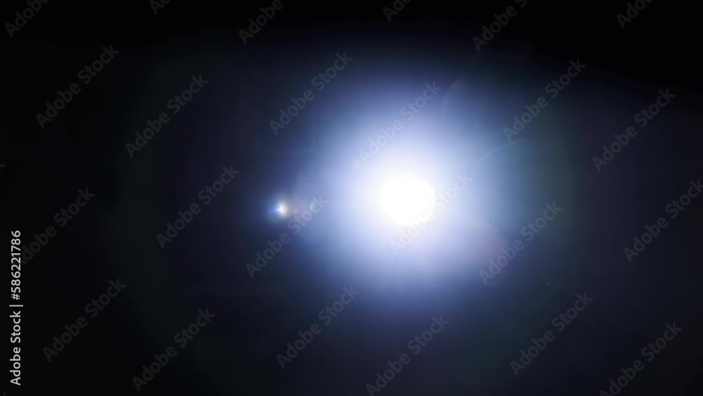 The light of a bright flashlight directed at the camera moves from side