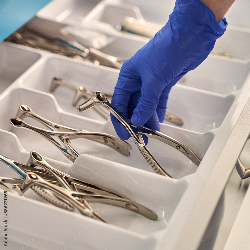 Doctor's hands wearing a disposable medical gloves holding a stainless steel nasal speculum for ENT examination over other surgery instruments