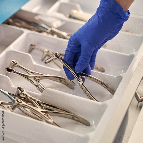 Obraz na płótnie Doctor's hands wearing a disposable medical gloves holding a stainless steel nasal speculum for ENT examination over other surgery instruments w salonie