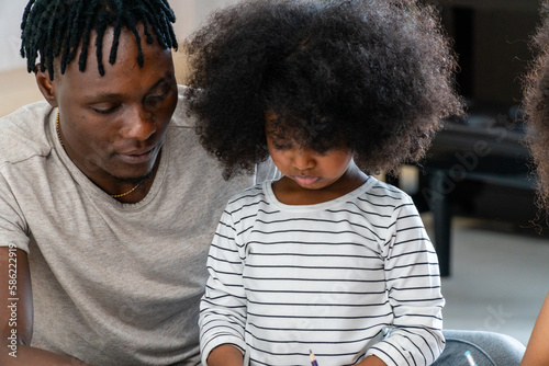 A black american father  his daughters are doing their homework in the living room.