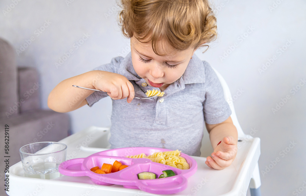 The child eats pasta and vegetables. Selective focus. The child eats pasta and vegetables. Selective focus.