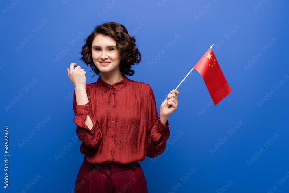 happy young student with curly hair looking at flag of China isolated on blue. happy young student with curly hair looking at flag of China isolated on blue.