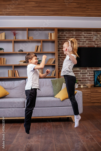 Children jump and dance at home while listening to music on headphones. Having fun. Family concept.