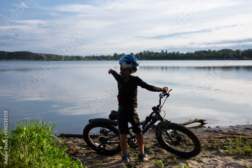 silhouette of little boy with bicycle on lake. concept of healthy active lifestyle, hobby. cycling, travel, summer vacation outside the city. scenery