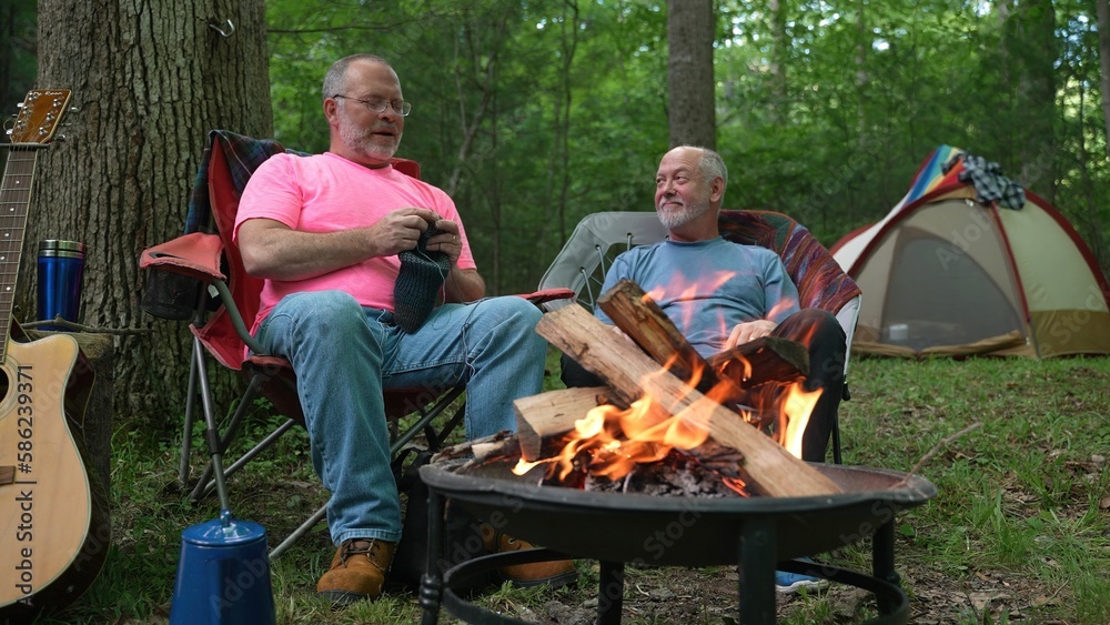 Obraz premium Two gay men sitting with each other, talking and smiling while sitting in front of a campfire in a forest.