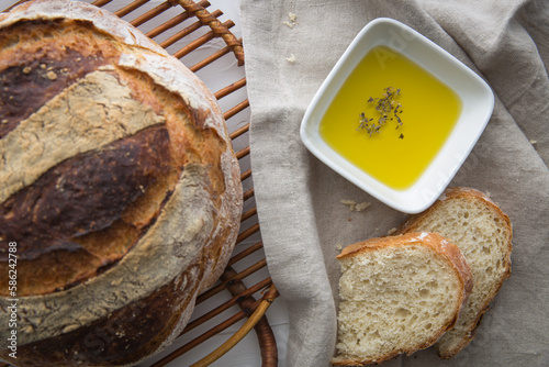 Close up of freshly baked round artisan bread with olive oil with oregano on the side.
