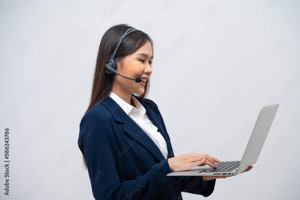 Beautiful Asian call center operator talking with customer using laptop isolated on grey background. Beautiful Asian call center operator talking with customer using laptop isolated on grey background.