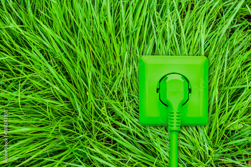 Grüne Steckdose mit Stromstecker und Kabel auf grünem Gras