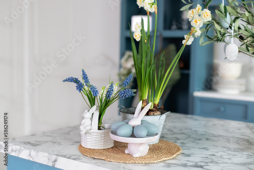 Daffodils in pot and spring flowers in vase. Home interior with easter decor. Bouquet of flowers in vase and ceramic plates, plants in pots, utensil on table in kitchen. Template