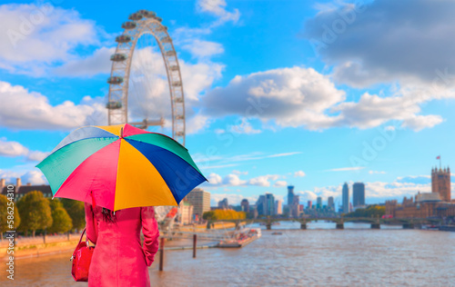 A woman in a red dress with a colorful umbrella stands and watches - Blured the London Eye on the river Thames  © muratart