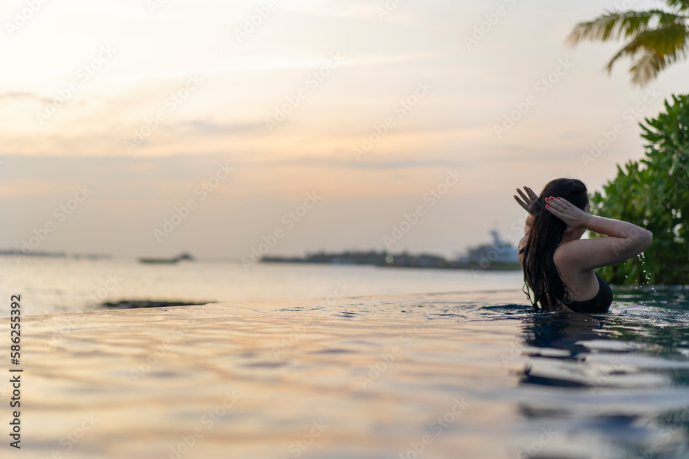 Young woman in the pool from the back at sunset straightens her hair Young woman in the pool from the back at sunset straightens her hair