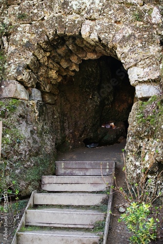 Fototapeta Naklejka Na Ścianę i Meble -  Cave entrance, wooden steps, moss on the rock and plants on the side