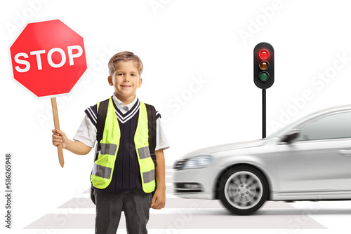 Schoolboy with a safety vest and a stop traffic sign standing at a pedestrian crossing with car driving