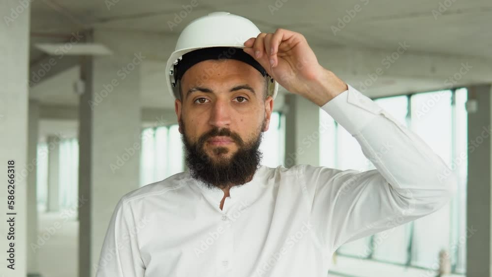 Confident Arabian Turkish civil engineer wearing a safety helmet looking at the camera, standing on construction site of office center